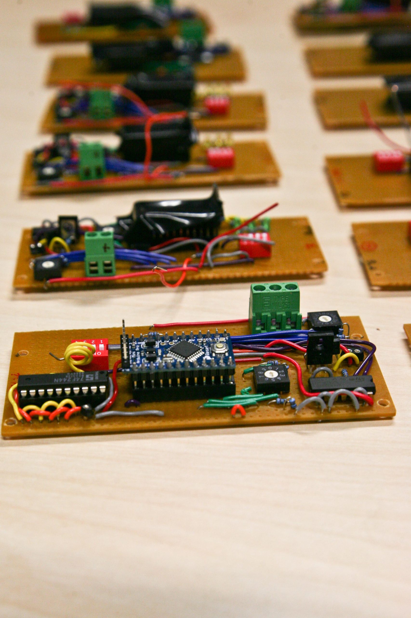 A photograph of electronic beacons laid out on a pine board showing their interiors that consist of multi coloured, red, green, blue, yellow, and grey wires connecting chips on circuit boards along with their other electronic components
