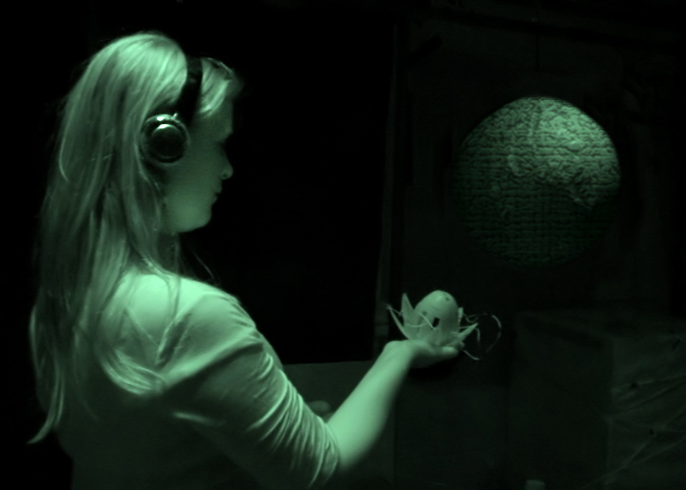 An infra red photograph of A young woman wearing headphones and holding a Lotus in her extended right hand moves towards a hanging sphere