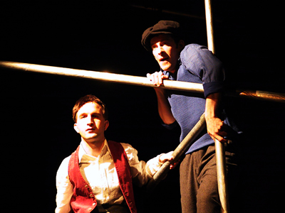 Young Jacques and Jean standing on top of the scaffold both looking out lit in an orange glow