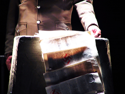 Close up of open report bearing a swastika emblem, its pages trailing over the podium