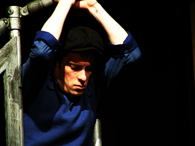 From the waist up, Jean in a blue jumper hangs from the scaffold by both arms