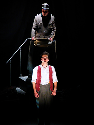 Up stage centre the Major is half lit on podium reading the report, with young Jacques down stage centre facing out in a brilliant white light against a dark background.