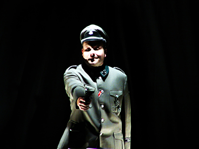 Waist up shot of Major lit from above pointing a gun straight out